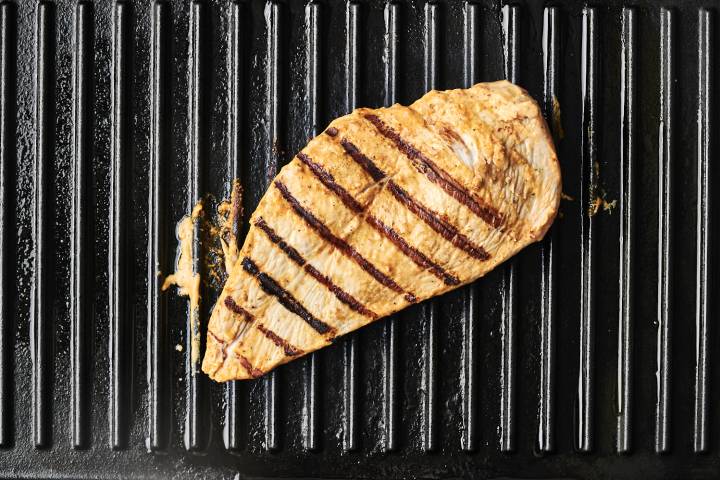 Grilled chicken breast with dark, defined grill marks sits on a black grill pan.